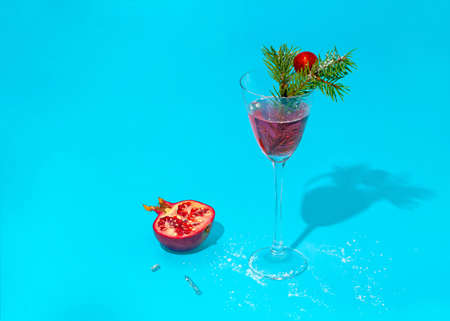 Modern cocktail glass with an exotic drink with small bubbles decorated with fresh green pine branches. Red decorative Christmas ball with pomegranate and glass shadow on a turquoise background.の写真素材