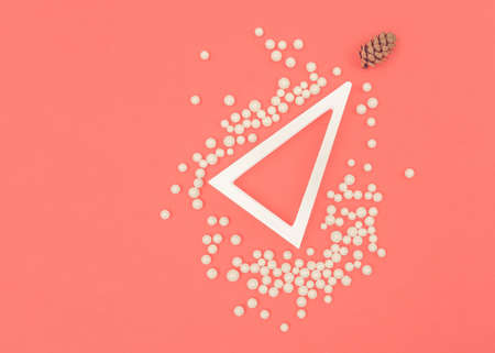 A modern Christmas concept. The simplicity of white and coral color. A white triangle as a Christmas tree. Copy space. Small white balls and a little cone. Asymmetric elements. New Year's event.の写真素材