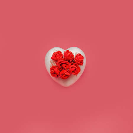 White heart with little red roses on a pastel coral color background. Creative love & flowers minimal concept. Beautiful present. Minimal Valentines Day. Anniversary concept. Flat lay.の写真素材