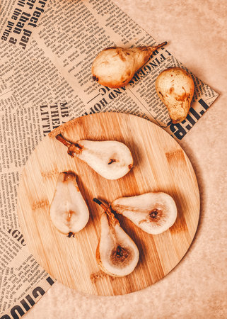 Rustic autumn concept. Retro, vintage idea. Juicy pears were cut in half and placed on a wooden bamboo board. Newspaper as decoration. Warm color tones, sharp edges of objects. Flat lay concept.の写真素材