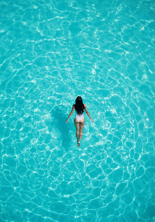 Aerial view of a young woman in bikini standing in a swimming poolの素材