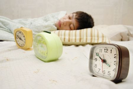 Sleeping boy at the morning and three alarm-clocksの写真素材