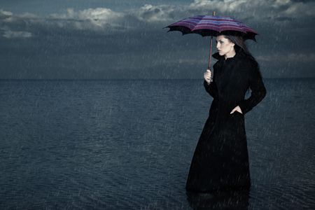 Lady with umbrella standing under the rain in the seaの写真素材