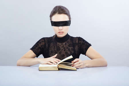 Woman with blindfold reading book indoorsの写真素材