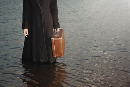 Torso of the woman in the black coat holding travel bag and standing in the waterの写真素材
