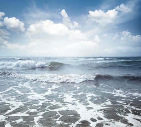 View on the blue sea with waves and spindrift under the cloudy skyの写真素材