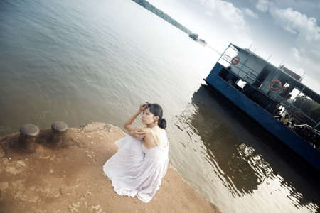 Sad lady at the wharf sitting and waiting. The floatboat on the backgroundの写真素材