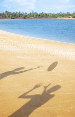 Shadows of two people playing with ball at the summer beach. Vertical photo with vibrant colorsの写真素材