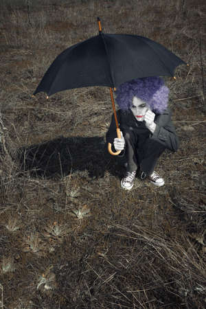 Alone funny man outdoors sitting and holding umbrella. Artistic color and darkness addedの写真素材