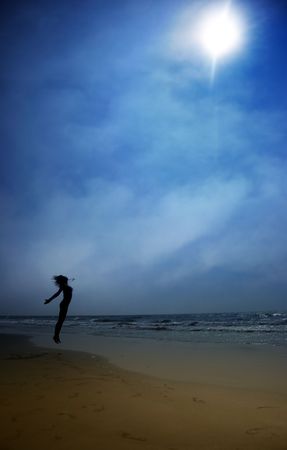 Silhouette of the jumping lady at the summer beach. Artistic colors and darkness addedの写真素材