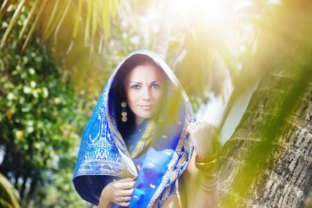Beautiful lady outdoors in stylish sari standing in the wild jungle under the sunlightの写真素材