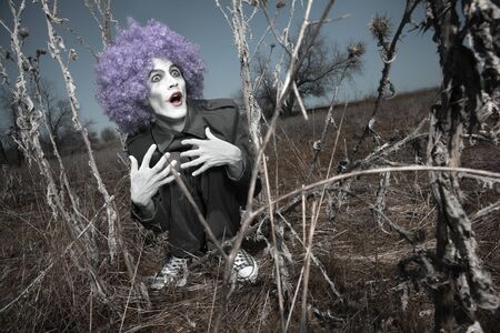 Crazy maniac clown outdoors hidden in the thorns. Artistic colors added