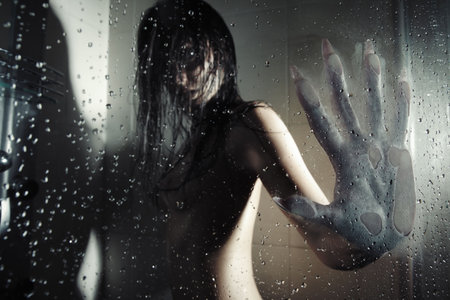 Female werewolf in the dark bathroom touching wet glass by his huge hand with sharp nails. Natural darkness. Artistic colors and grain addedの写真素材