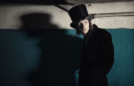 Criminal man in vintage black coat and top hat in the dark interior. Natural darkness and colorsの写真素材