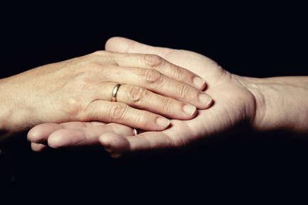 Two hands of senior people with engagement rings on a black backgroundの写真素材
