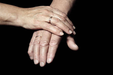 Two hands of senior people with engagement rings on a black backgroundの写真素材