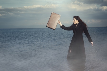 Bizarre female traveller with bag standing in the water with fog. Natural light and colorsの写真素材