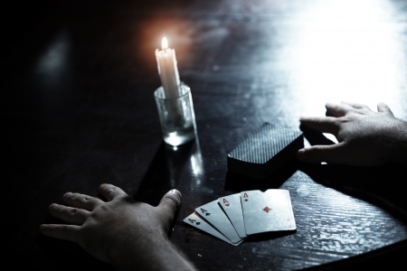 Human hands on a dark table with pack of cards and flaming candleの写真素材