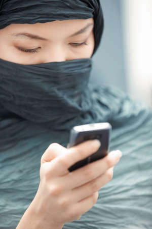 Oriental lady in hijab sending SMS via cell phoneの写真素材