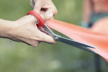 Hands of female tailor cutting red ribbon. Close-up viewの写真素材