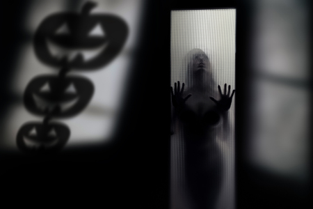 Silhouette of the woman behind the wall with Halloween pumpkin shadesの写真素材