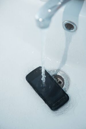 Smartphone in sink with flowing water. Vertical photoの写真素材
