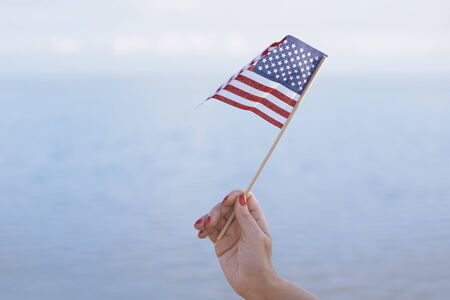 Woman hand holding USA flag in front of the ocean