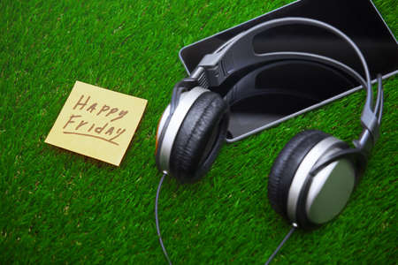 Happy Friday text on sticky note on a grass with headphones and digital tabletの写真素材