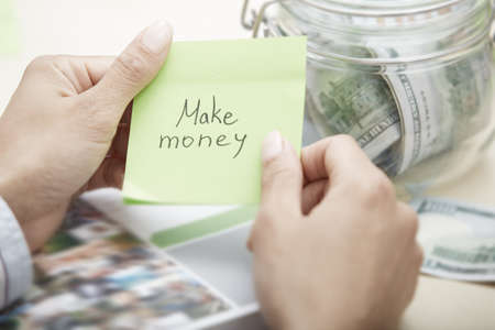 Hands of businessperson holding adhesive note with Make money text