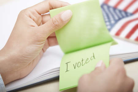 Human hands holding adhesive note with I voted text