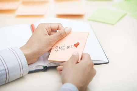 Hands holding sticky note with SMS me text