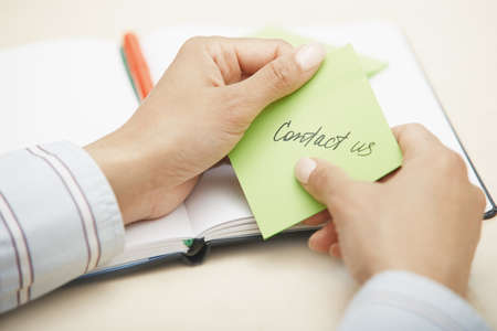 Hands holding sticky note with Contact us textの写真素材