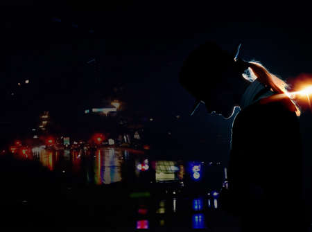 Silhouette of the woman with hat standing in the night city with illuminationの写真素材