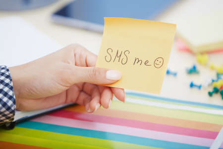 Human hand holding adhesive note with SMS me text