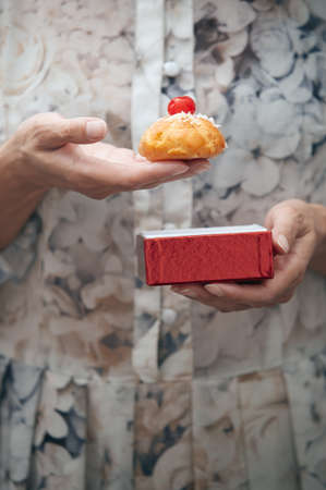Woman holding eclair and red box. Vertical photoの写真素材