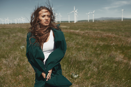 Woman with long tousled hair next to the wind turbine with the wind blowingの写真素材