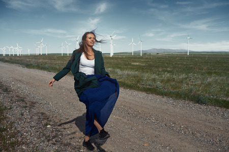 Woman with long tousled hair next to the wind turbine with the wind blowingの写真素材