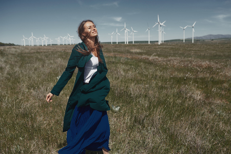 Woman with long tousled hair next to the wind turbine with the wind blowingの写真素材