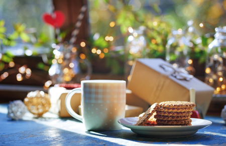 Teacup and Christmas gluten free cookies on a table near the decorated window with gift boxesの写真素材