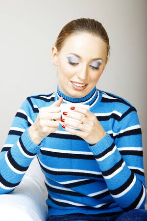 Smiling woman indoors in striped sweater holding cup with tea or coffeeの写真素材