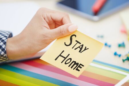 Human hand holding adhesive note with Stay Home textの写真素材