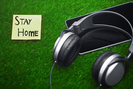 Stay Home text on sticky note on a grass with headphones and digital tabletの写真素材