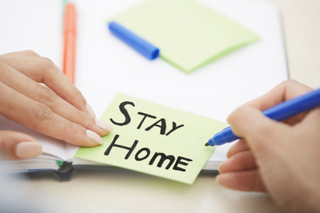Hands of woman writing on adhesive note with Stay Home textの写真素材