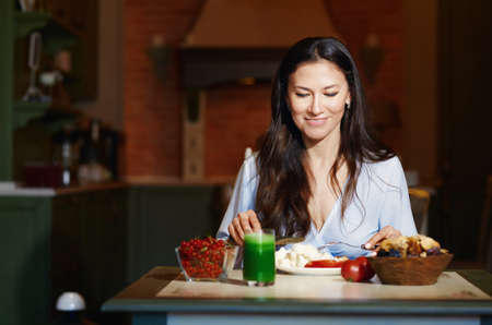 Smiling vegetarian woman sitting at the table and eating healthy foodの写真素材