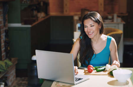 Woman at the table with vegetables working via laptopの写真素材