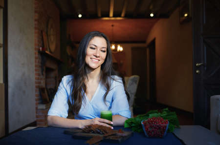 Smiling vegetarian woman sitting at the table with celery fresh juice, flaxseed bread and berriesの写真素材