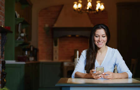 Smiling woman sitting and table and using smartphoneの写真素材