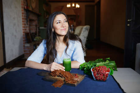 Smiling vegetarian woman sitting at the table with celery fresh juice, flaxseed bread and berriesの写真素材