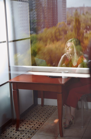 Young adult woman sitting at the table and working on laptopの写真素材