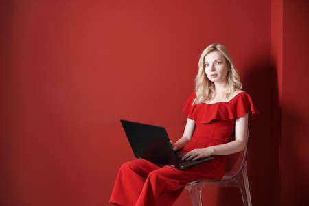 Young adult woman sitting on a chair and working on laptopの写真素材